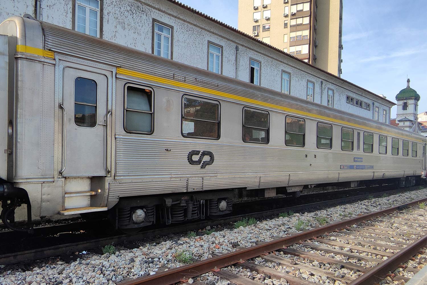 1st class Sorefame coach with gray livery and a yellow stripe above the windows stopped at the station.