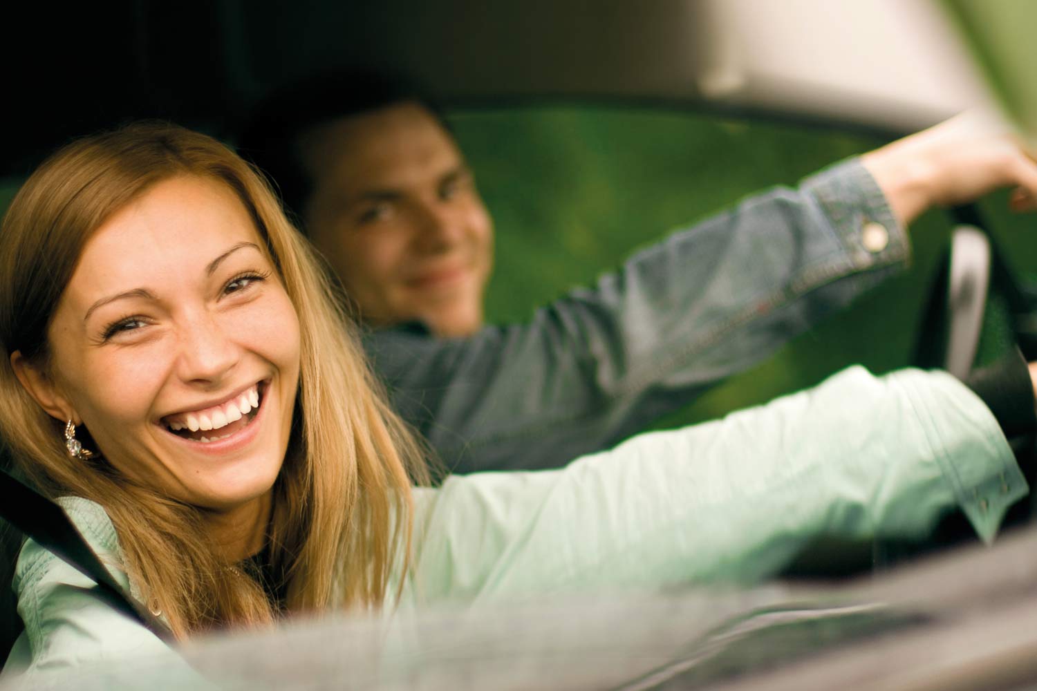  Woman and man sitting in the front seats of a car, smiling as they look out the window 