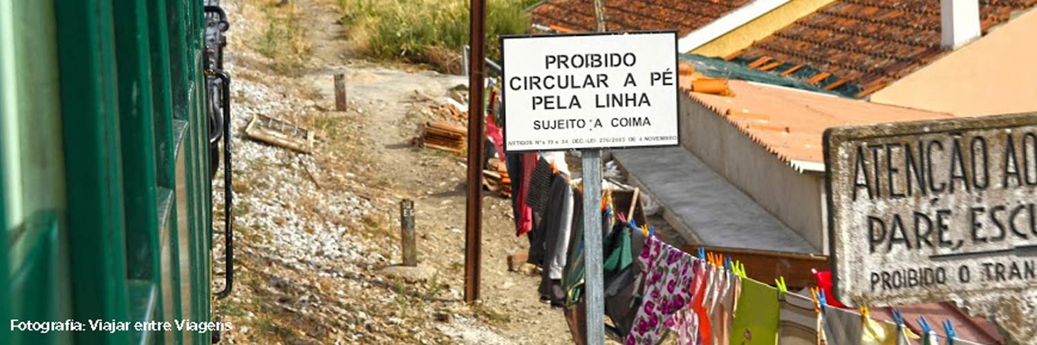 Sinalização que alerta para passagem de comboio junto à linha, entre uma casa e o comboio a passar.