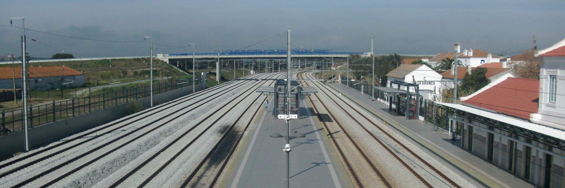 Vista da passagem superior para peões na Estação de Casa Branca, com plataformas, linhas, edifício da estação e ao fundo um viaduto de uma estrada sobre as linhas.