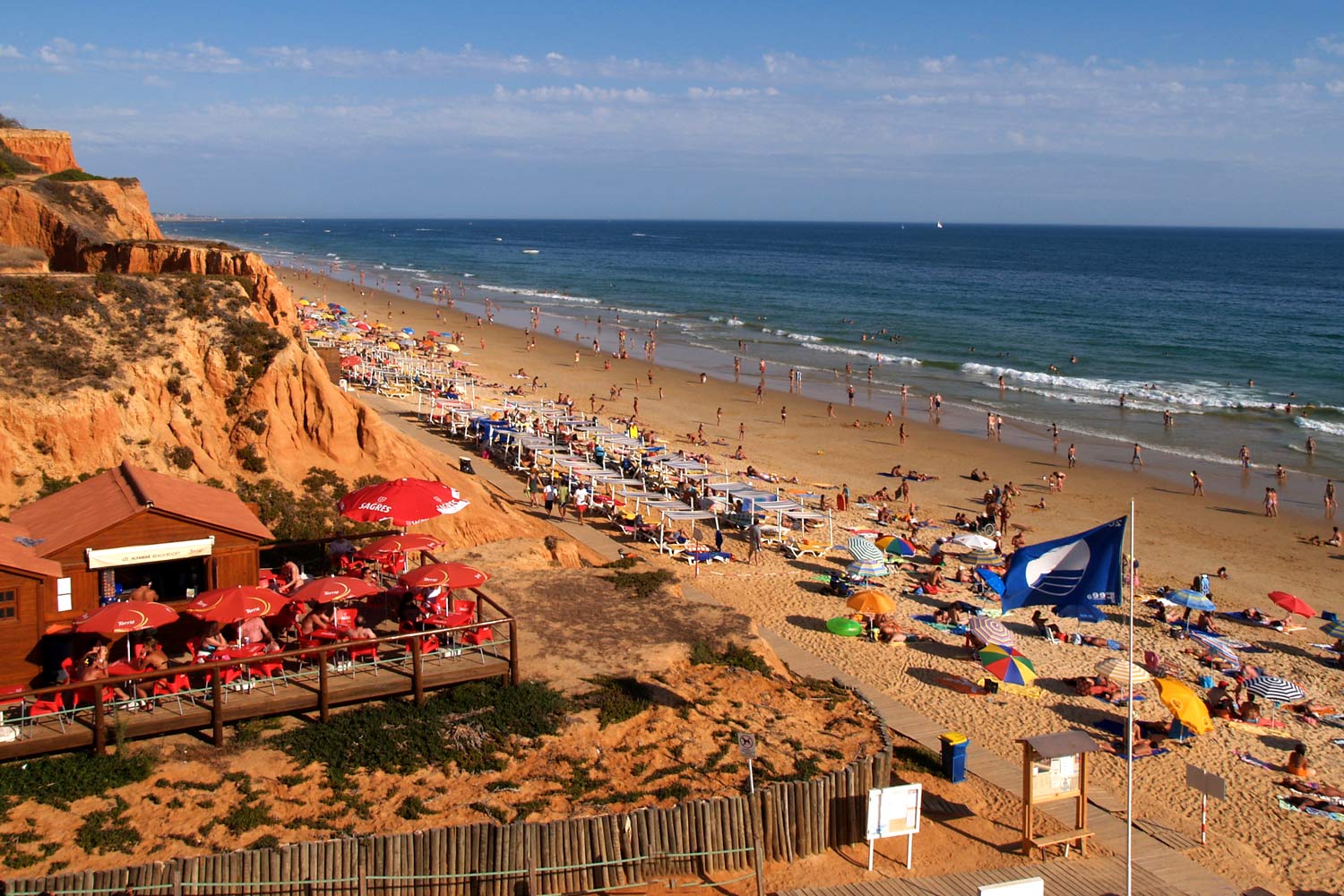 Praia da Falésia, em Albufeira, com pessoas em espreguiçadeiras e guarda-sóis e o bar de praia com esplanada.