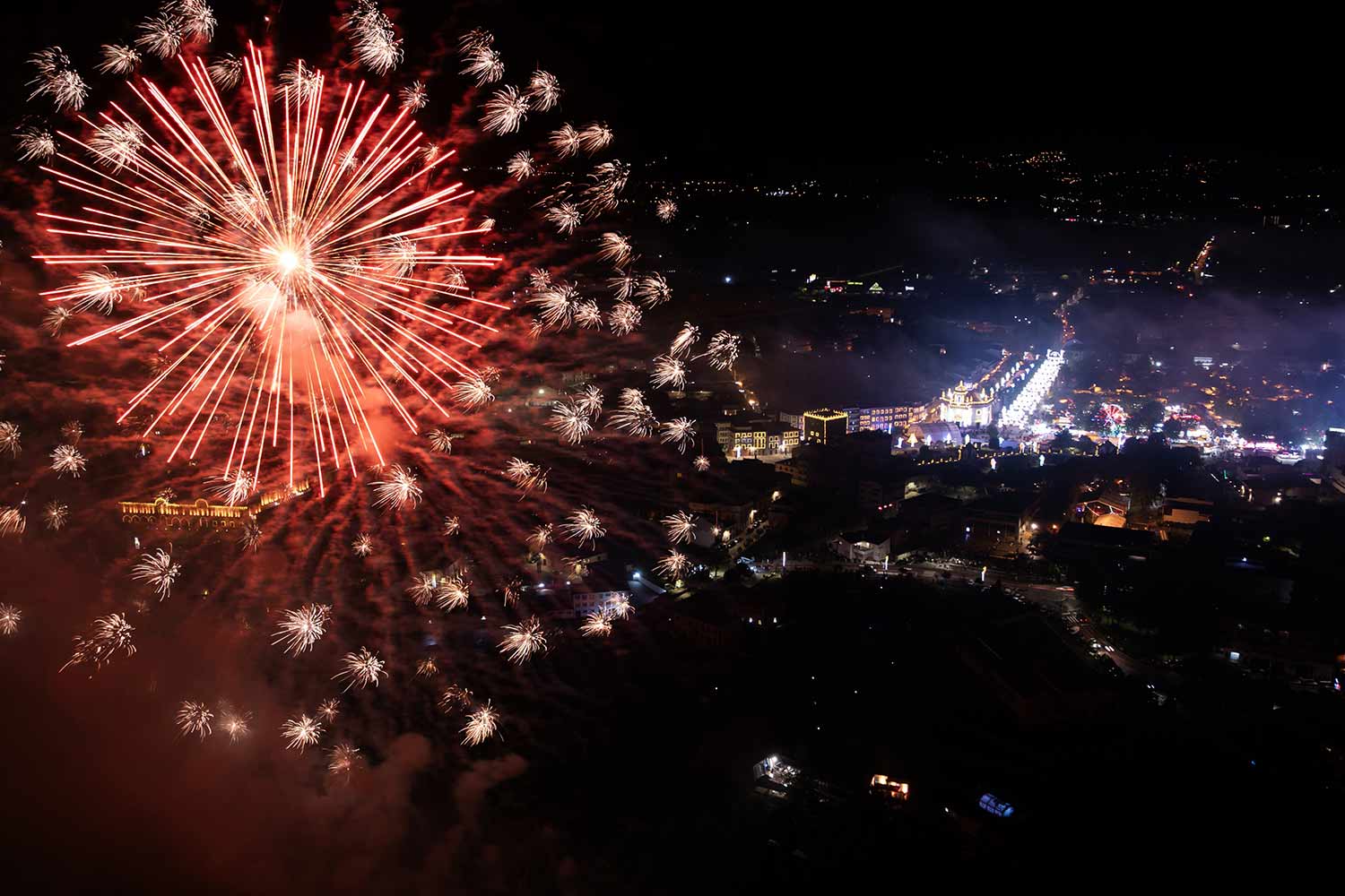 Imagem aérea  noturna da cidade de Barcelos, iluminada e com fogos de artifício da festa.