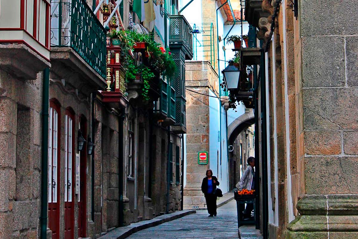 rua no centro histórico com edifícios com floreiras penduradas nas varandas e uma senhora a caminhar