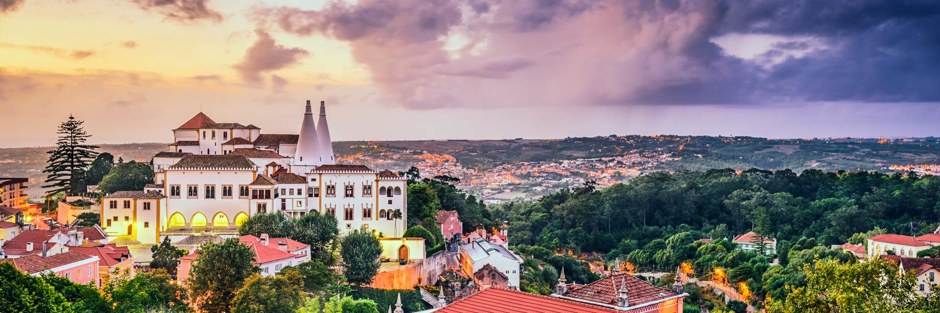 Vista do Palácio Nacional de Sintra, alguns telhados e área verde, em luz de final de tarde.