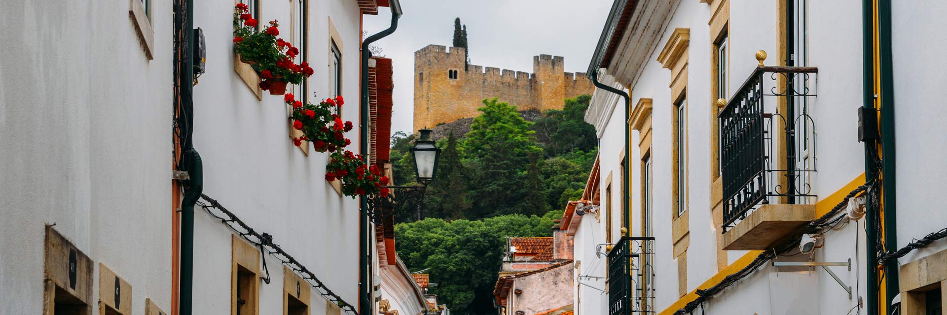 Janelas e sacadas numa rua com vista para uma parte da muralha do Convento de Cristo.