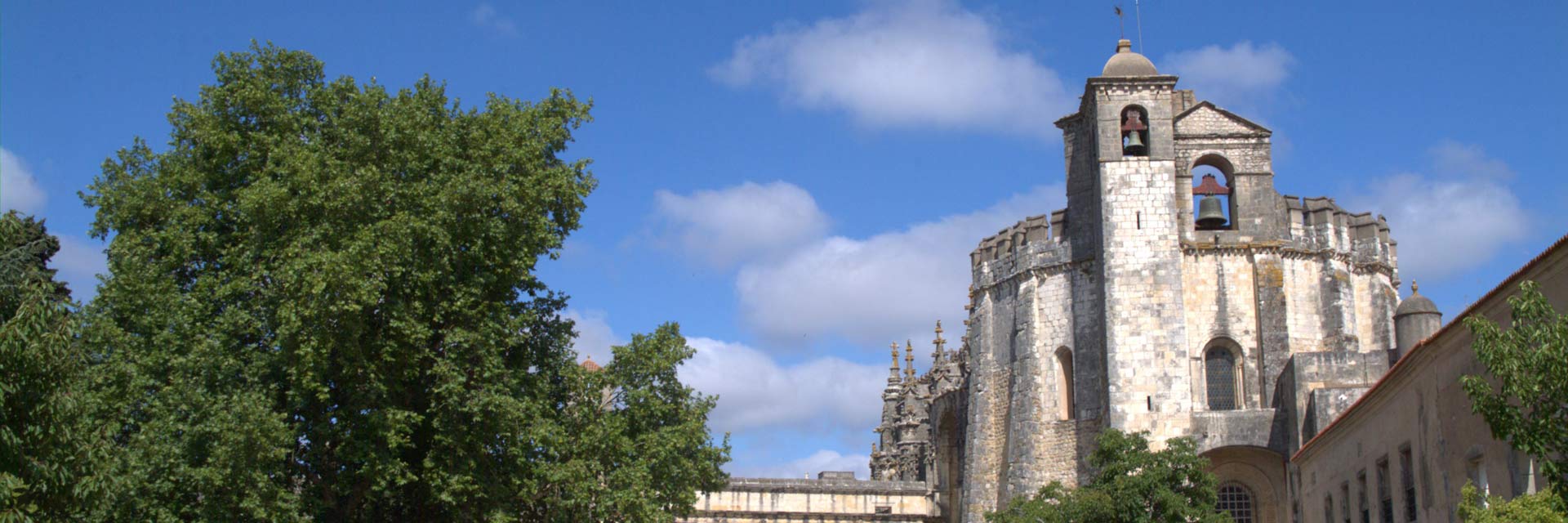 Igreja do Convento de Cristo com duas torres com sinos e uma frondosa árvore.
