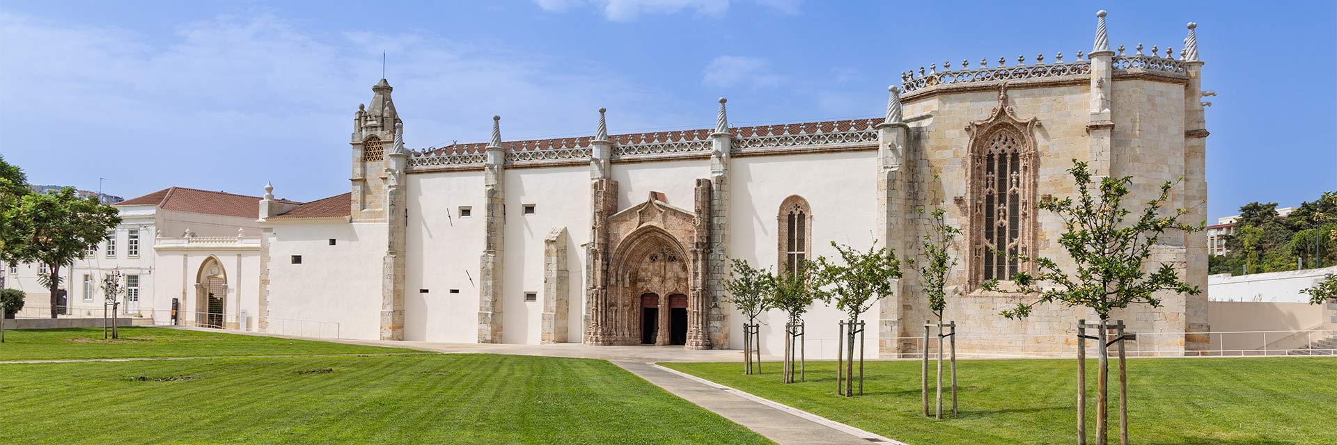 Imagem a cores do exterior do Convento de Jesus, com área ajardinada com relva e árvores.