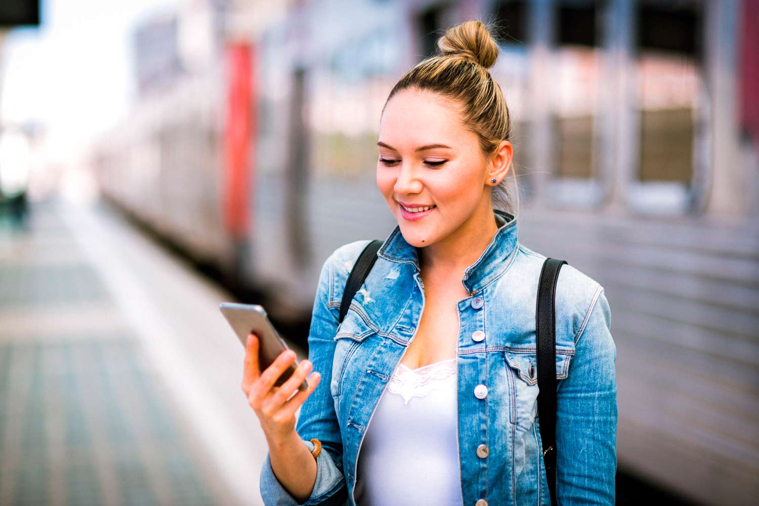 A picture of a young girl standing next to a commuter train, checking information on a mobile phone.