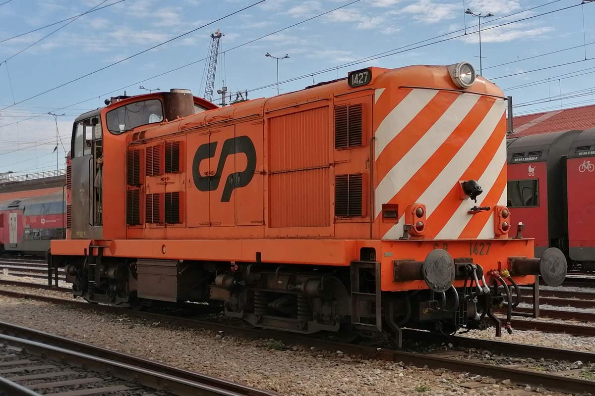 Locomotiva da série CP 1400 cor laranja e com listras brancas na frente, parada numa das linhas da estação.