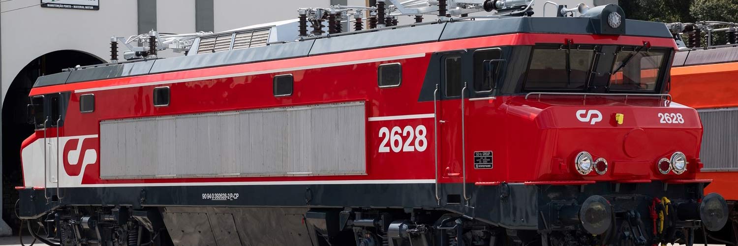 Locomotiva da série CP 2620 cor vermelho, parada em frente às oficinas.