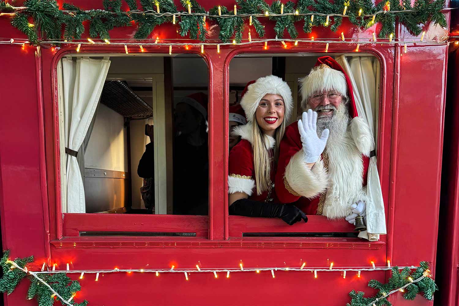 Mãe Natal e Pai Natal a acenar na janela do comboio decorado com luzes de Natal