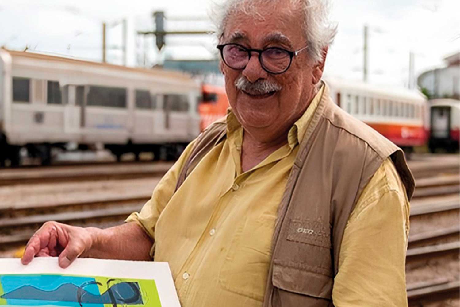 Imagem a cores de José Manuel Ludovice Santa Bárbara, nas Oficinas de Contumil, com carruagens e locomotiva elétrica em pano de fundo.