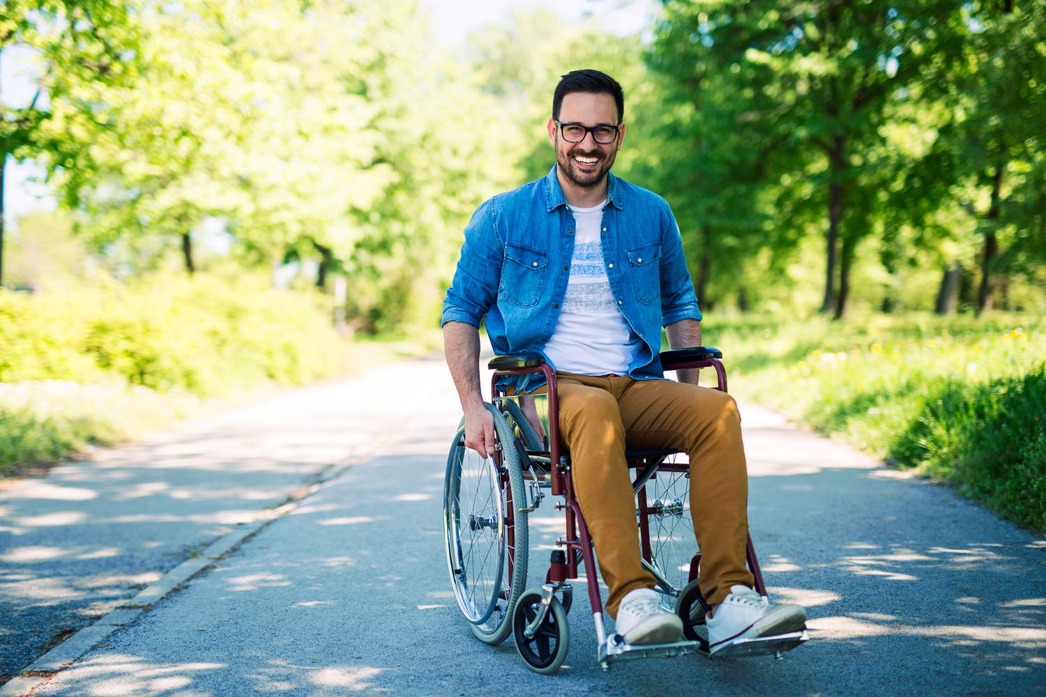  Smiling man in a wheelchair, with trees and vegetation in the background.
      