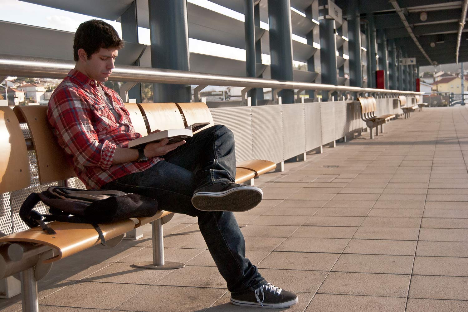 Jovem a ler, sentado em banco da plataforma da estação.