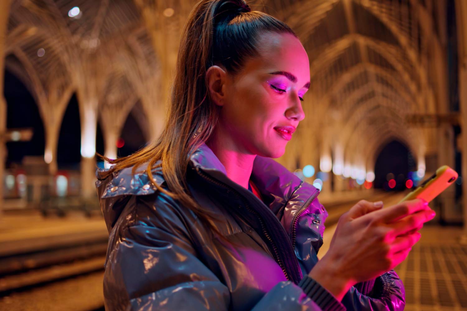Woman looking at a smartphone at night on the platform of Oriente station.