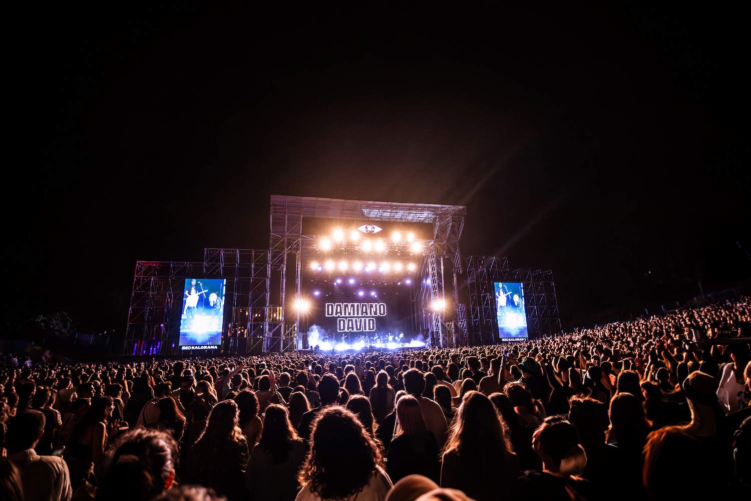 Imagem noturna de pessoas junto a palco, com banda a atuar.