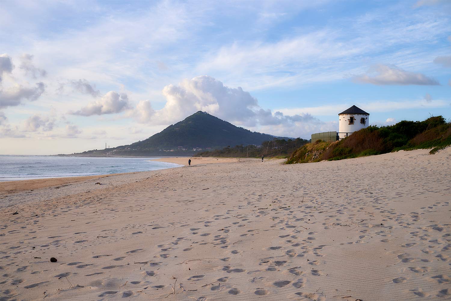 Imagem a cores do mar e do areal vazio, com o Monte de Santa Tecla ao fundo.