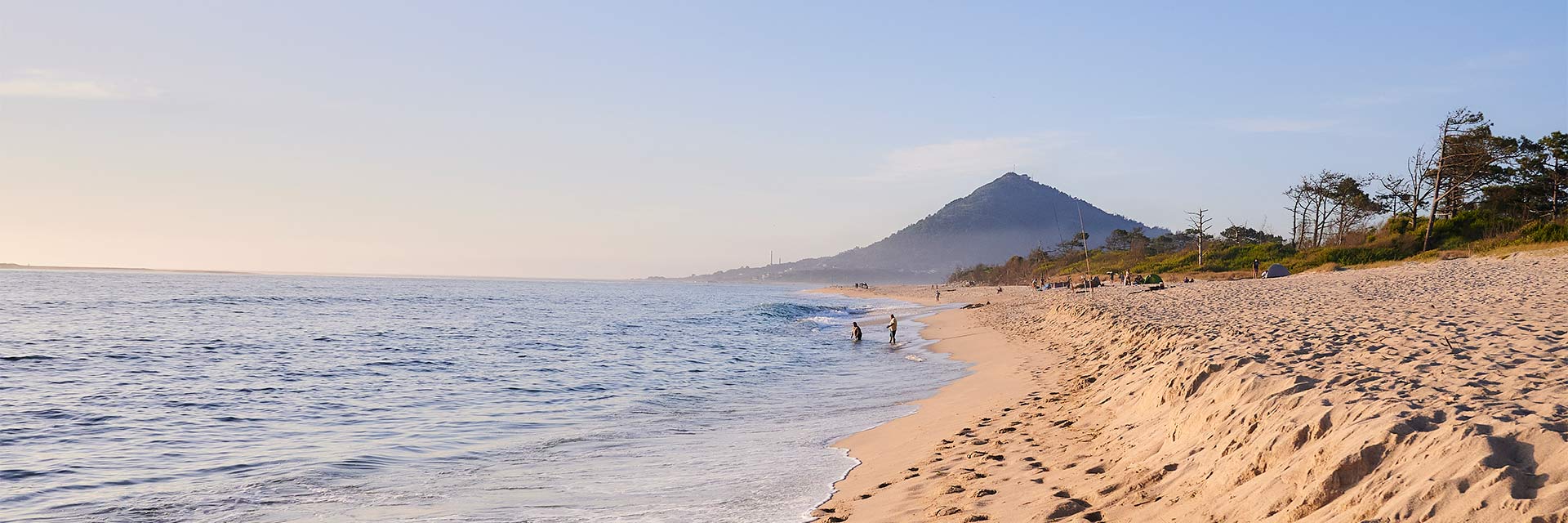 Imagem a cores do mar, com pessoas a ir a banhos e com o Monte de Santa Tecla ao fundo.