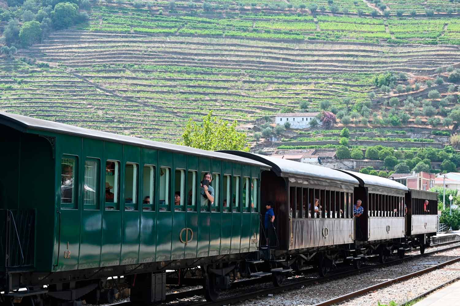 Carruagens históricas de madeira com pessoas a janela, e ao fundo a paisagem dos socalcos do Douro.