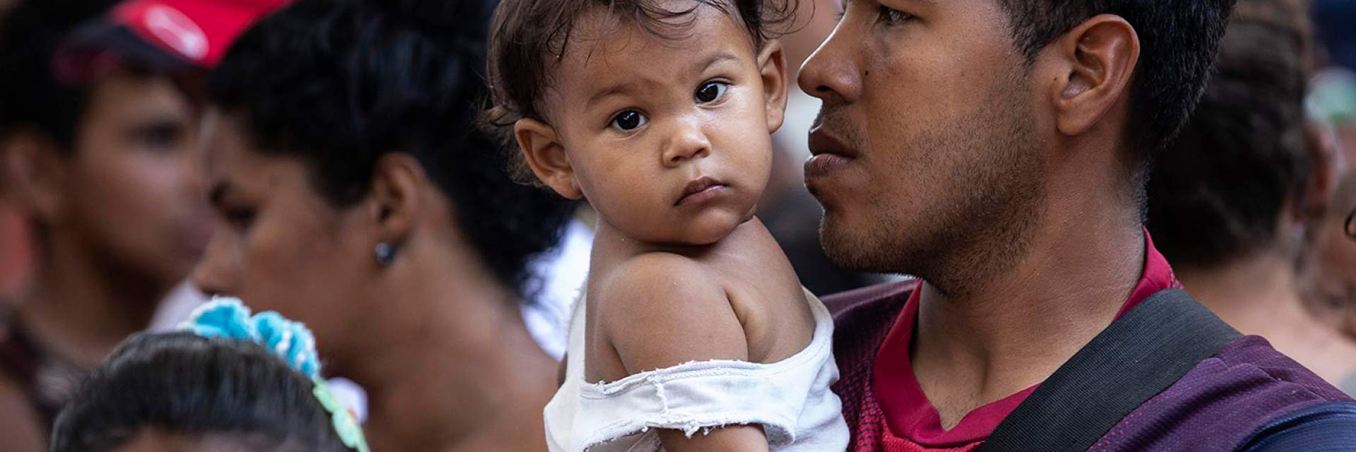 Man holding a baby in his arms, waiting with other people.